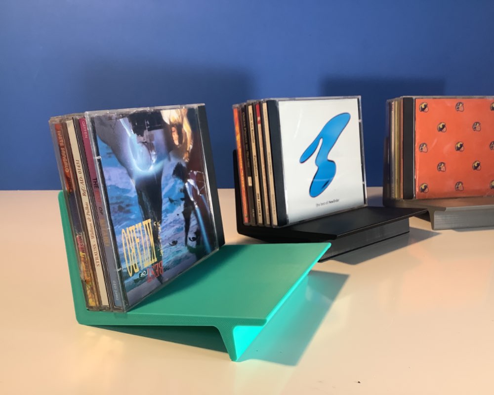 three colorful CD racks, turquoise, black and grey, holding varios compact disk cases