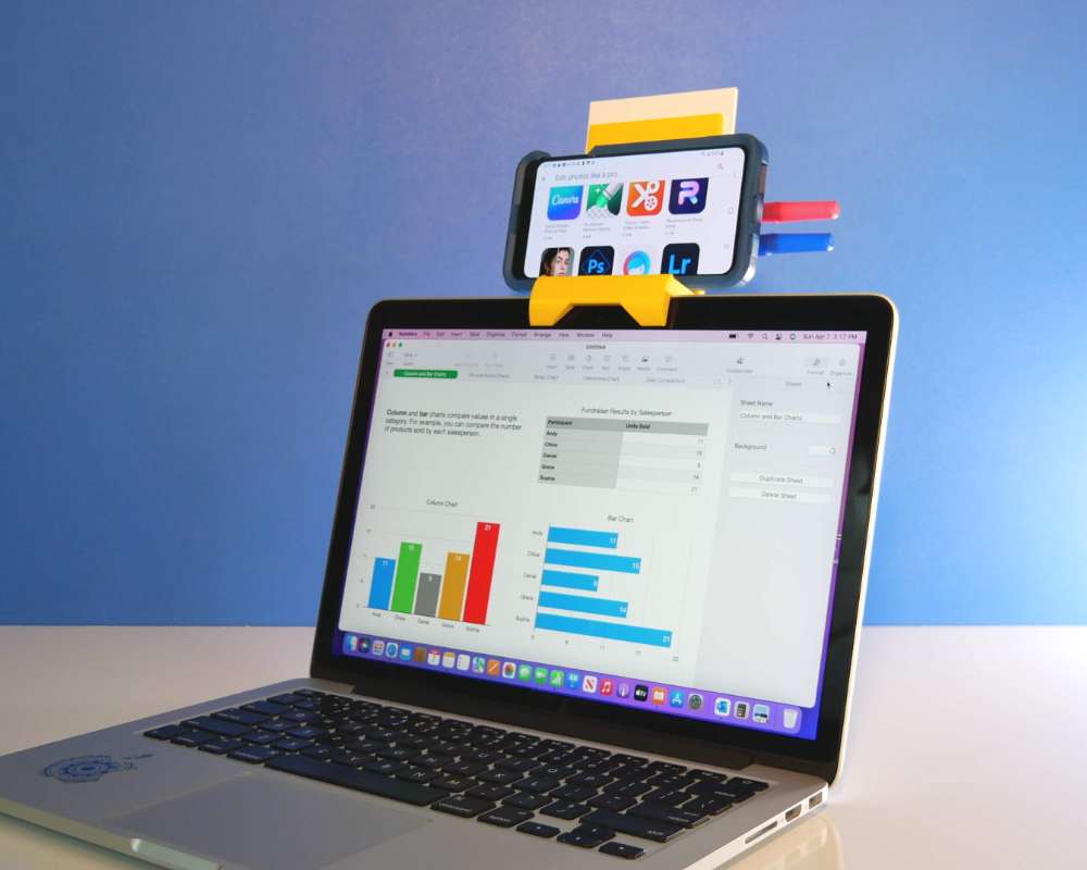 a plastic stand holding a mobile phone on top of a laptop computer screen
